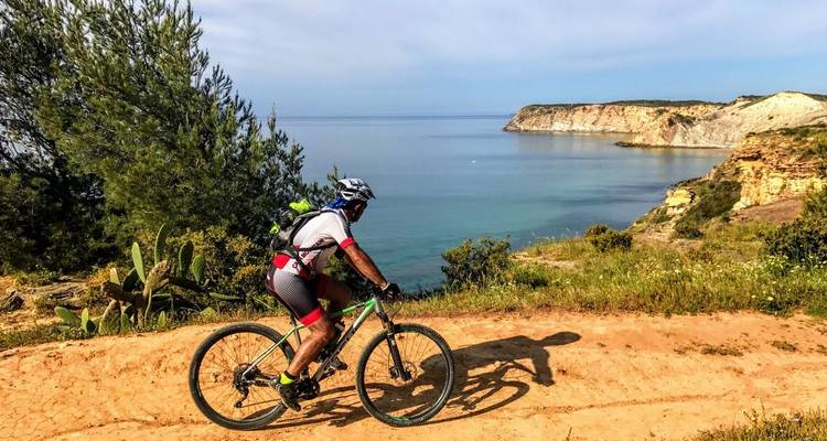 Mountainbiker op een kustpad van aarde met uitzicht op turquoise zee en ruige rotsen