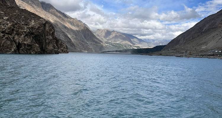 Amplio lago azul enmarcado por picos áridos y nubes dispersas.