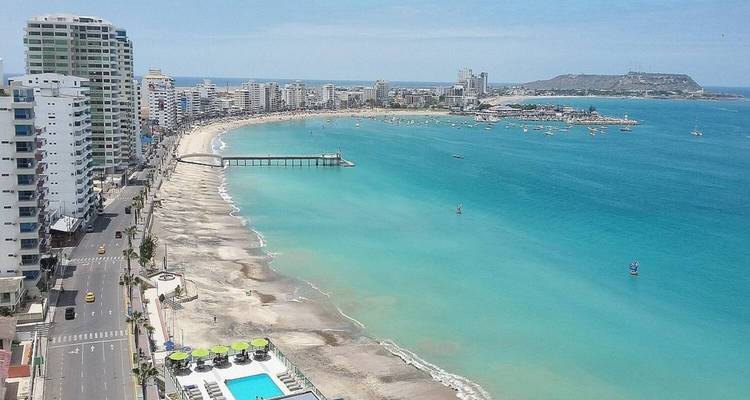 Aerial view of turquoise sea and long curved urban beach backed by high-rise skyline.
