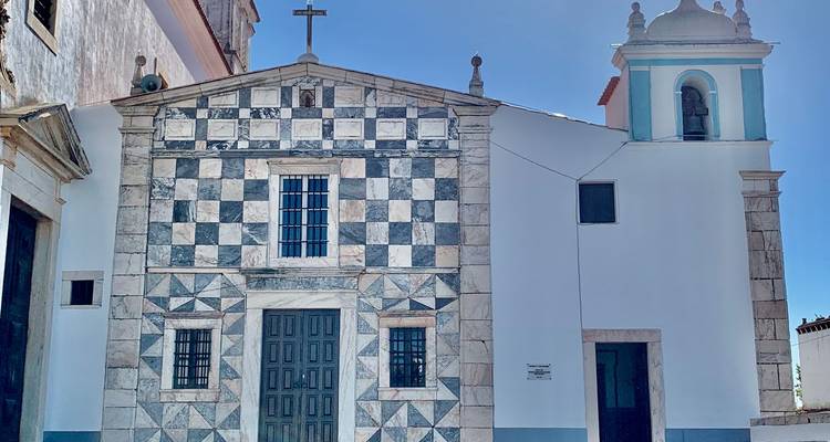 Fachada de iglesia decorada con distintivos patrones de mármol ajedrezado en blanco y negro y una pequeña torre campanario.