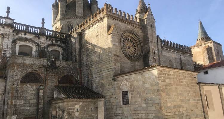Catedral gótica de piedra con torres masivas, rosetón y almenas iluminada por cálida luz solar.