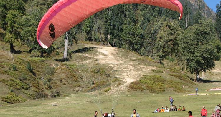 Tandem paraglider lifts off from a grassy alpine meadow while onlookers watch from below.