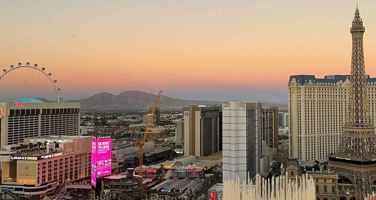 Panoramic dusk view of Las Vegas Strip skyline with hotels, Ferris wheel and distant mountains under pastel sky.