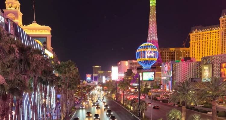 Nighttime scene along brightly lit Las Vegas Boulevard with neon lights, hotels and streams of car headlights.