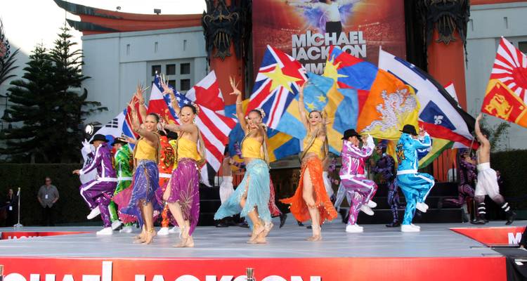 Energieke podiumvoorstelling met dansers in kleurrijke kostuums die internationale vlaggen zwaaien bij een Michael Jackson-show.