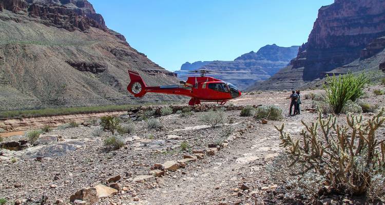 Un helicóptero rojo aterrizó en el piso rocoso de un cañón con un viajero solitario parado cerca.