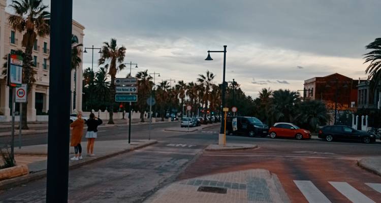 Rue du soir près de la côte valencienne avec des palmiers, des voitures et deux piétons qui prennent des photos