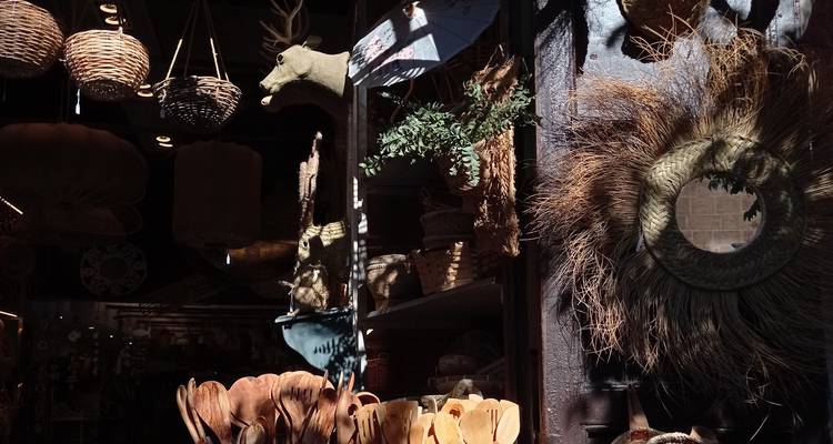 Vitrine de boutique éclectique remplie de paniers, de couronnes et d'objets artisanaux en bois sous un fort ensoleillement