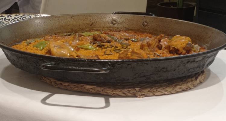 Paella valencienne traditionnelle dans une grande poêle en fer sur un dessous-de-plat tissé prêt à être servi