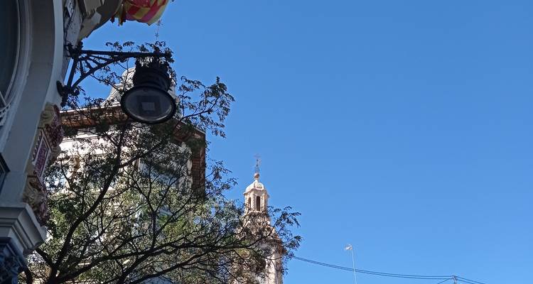 Scène de rue avec lampadaire orné, branches d'arbre feuillues et clocher d'église se détachant sur un ciel bleu dégagé