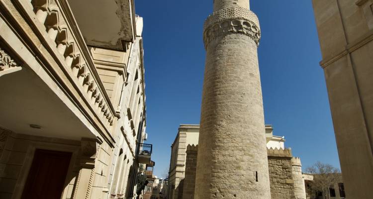 Rue étroite de la vieille ville de Bakou dominée par un haut minaret de pierre et des bâtiments historiques.