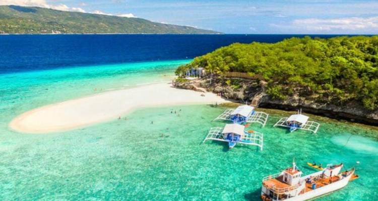 Vista aérea de una isla de banco de arena prístina rodeada de agua turquesa vívida y barcos anclados.