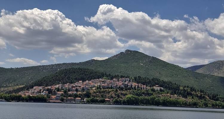 Hillside town with red-tiled roofs beside a tranquil lake backed by green mountains and clouds