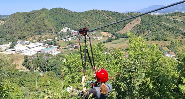 Person wearing red helmet riding a zipline over a lush green valley and town