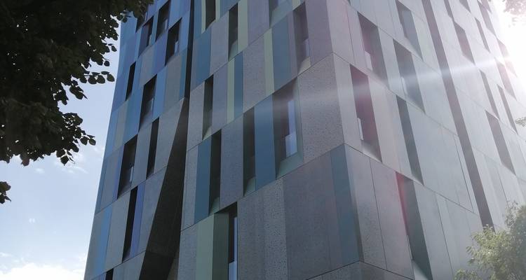 Tall contemporary building with patterned facade and dramatic sun flare viewed from below