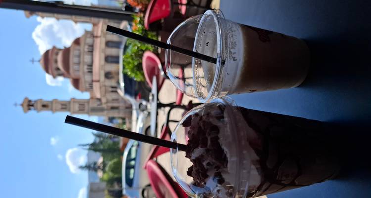 Two iced coffee drinks on a café table with a blurred view of a cathedral in the background