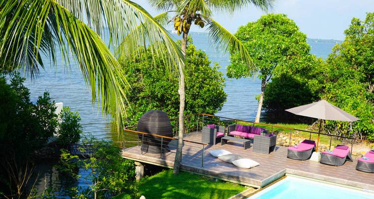 Terrasse privée avec canapés de salon magenta à côté de la piscine donnant sur le lagon bleu et les palmiers.