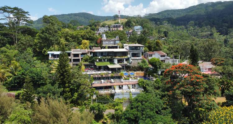 Vue aérienne du village montagnard en étages avec ses maisons, sa végétation et sa tour de télécommunications au sommet.