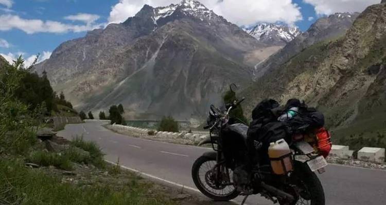 Beladenes Tourenmotorrad geparkt neben einer kurvigen Alpenstraße mit sich auftürmenden Felsgipfeln dahinter.