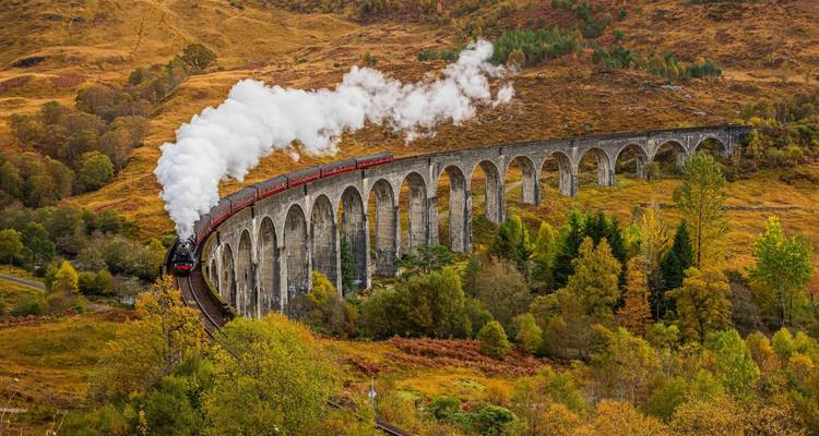 The Jacobite steam train puffs across the Glenfinnan Viaduct amid autumnal Highlands scenery.