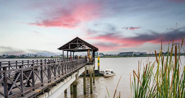Wooden riverside pier at dusk with vivid pink and purple sunset clouds over the city