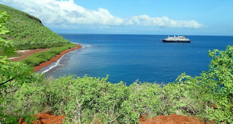 Expedition cruise ship anchored off a lush volcanic island in vivid blue sea