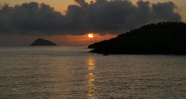 Sunset over calm sea with fiery orange reflection and silhouetted island