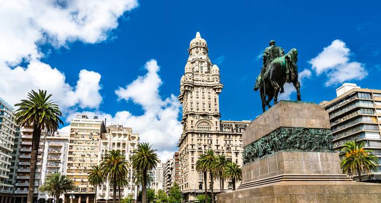 Reiterstatue von General Artigas überblickt die Plaza Independencia mit Palacio Salvo und Palmen unter einem leuchtend blauen Himmel.