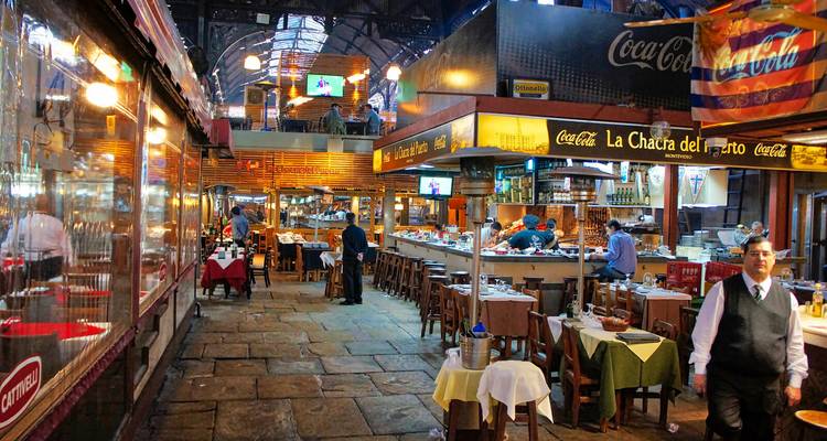 Lebhafter überdachter Grillmarkt mit Gästen an Holztischen und Köchen, die unter warmem Licht Speisen zubereiten.