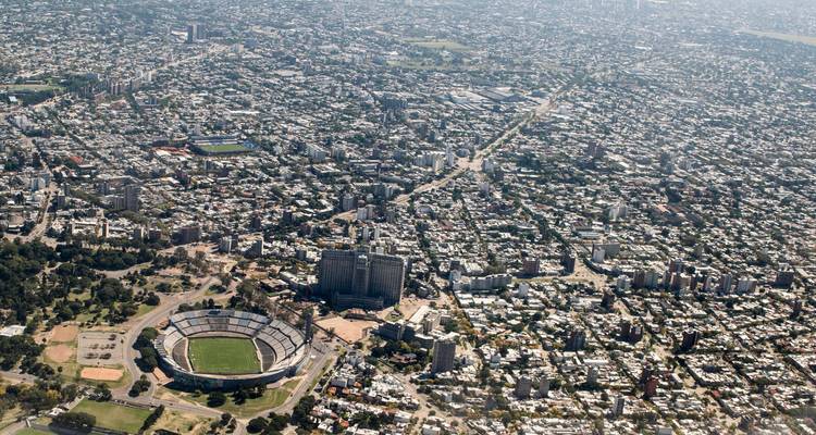Luftpanorama einer weitläufigen Stadt mit großem Fußballstadion und gitterförmigem Straßennetz.