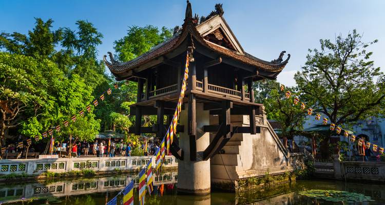 Historische Eenzuilpagode die uittorent boven een kleine vijver met bezoekende toeristen en kleurrijke gebedsvlaggen.