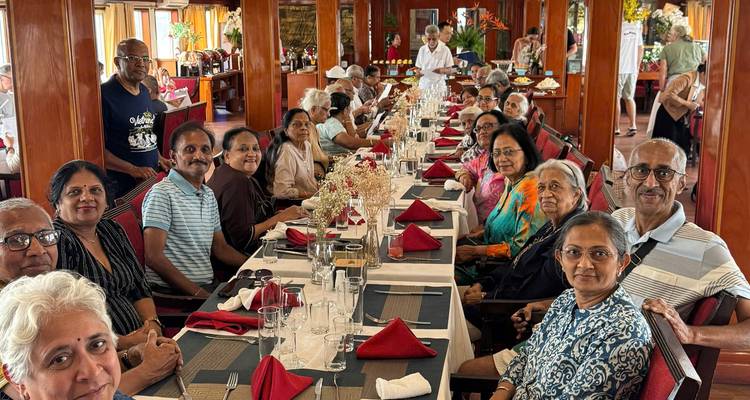 Lange tafel gedekt voor de lunch in een cruise-eetzaal met een grote groep volwassen reizigers die naar de camera glimlachen.