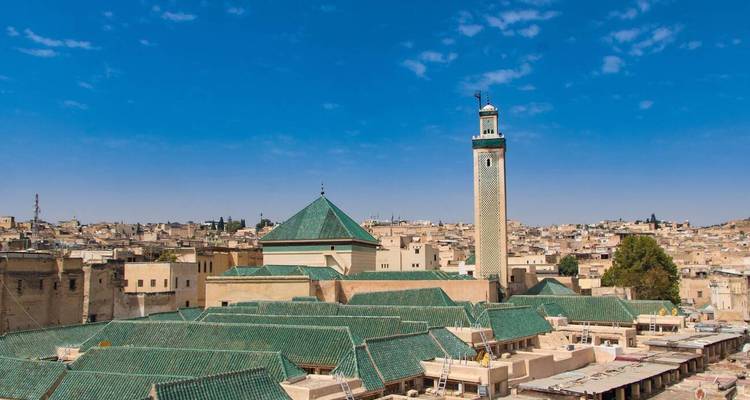 Panorama de l'horizon de Fès avec des toits aux tuiles vertes et un minaret élancé sous un ciel bleu éclatant.