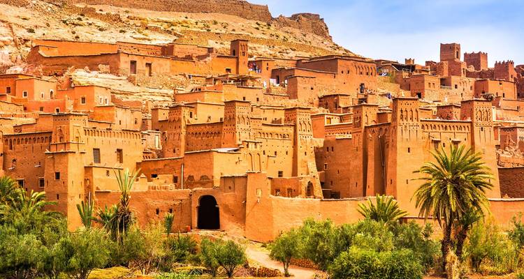 El ksar fortificado de tierra de Ait Benhaddou se eleva sobre un frondoso oasis de palmeras bajo un cielo despejado.