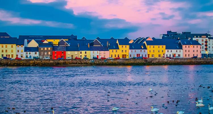 Rangée de maisons colorées connue sous le nom de la Promenade Longue se reflétant dans le port de Galway au crépuscule avec des oiseaux sur l'eau