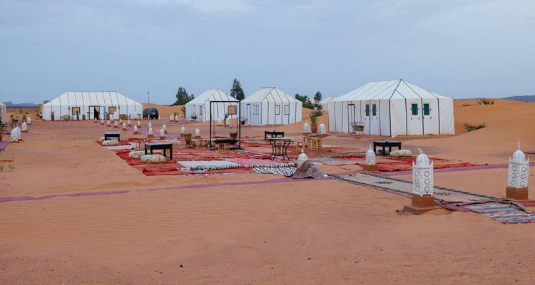 Vue large de tentes de désert en toile blanche et de tables basses disposées sur des tapis rouges dans les dunes du Sahara