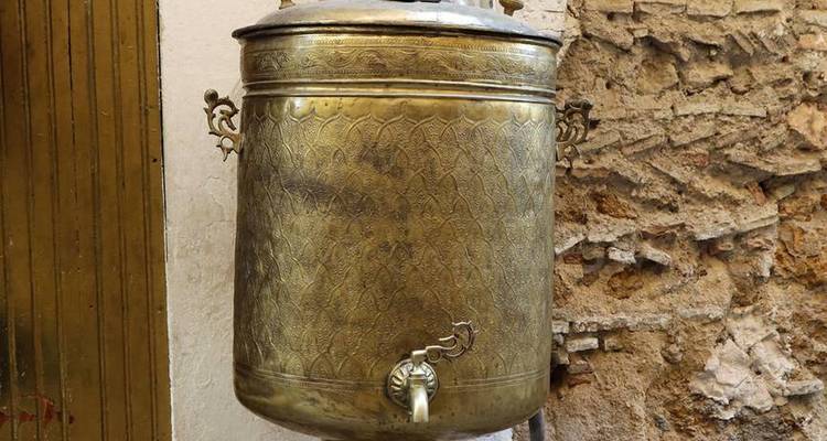 Urne à eau en laiton antique avec motif orné montée sur un mur dans une médina marocaine
