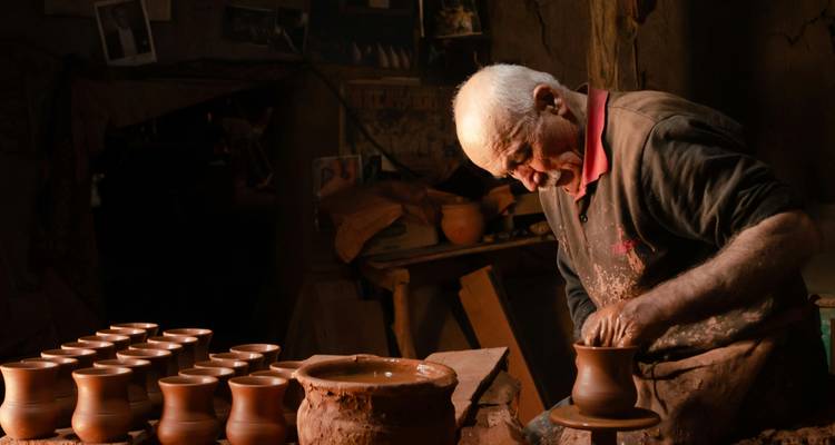 Artesano anciano moldeando arcilla en un torno de alfarería en un taller cálido.