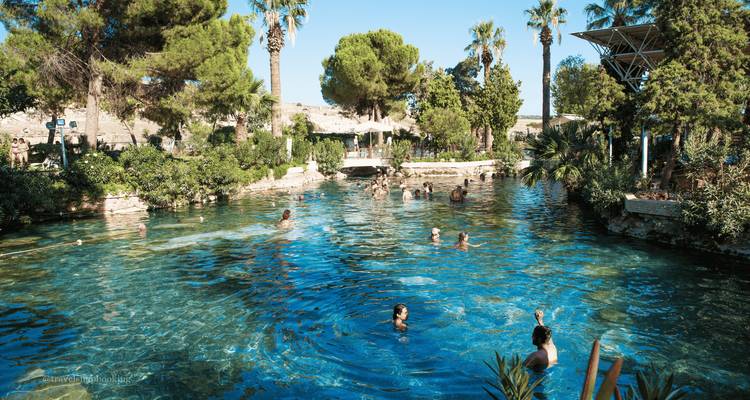 Personas nadando in una piscina termal natural cristalina rodeada de palmeras en Pamukkale.