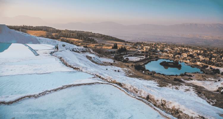 Vista panorámica de las piscinas escalonadas de travertino blanco de Pamukkale con vista al pueblo y la llanura al atardecer.