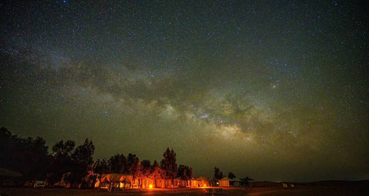 Ciel nocturne étoilé avec la Voie lactée formant une arche au-dessus de tentes de glamping du désert doucement éclairées