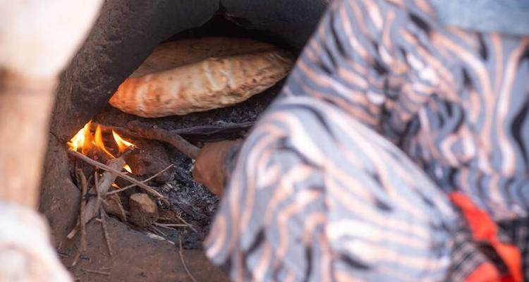 Vue rapprochée de pain plat traditionnel cuisant dans un four en argile au-dessus d'une petite flamme nue