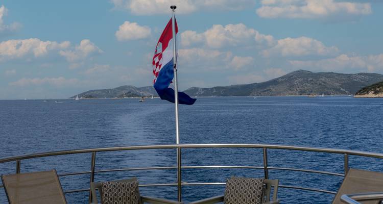 Kroatische vlag die flatert aan de achterkant van de boot met een lang spoor door de blauwe Adriatische Zee erachter.