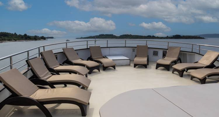 Circulaire opstelling van beige ligbedden op het open zonnedek van het schip met uitzicht op kalm grijs-blauw water.