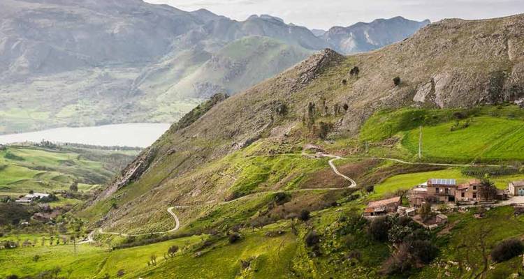Uitgestrekte groene vallei met slingerende wegen, verspreide huizen en een veraf gelegen meer onder bergen.