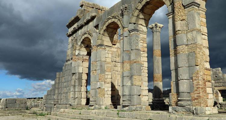 Arches et colonnes de pierre anciennes des ruines romaines de Volubilis sous des nuages dramatiques.