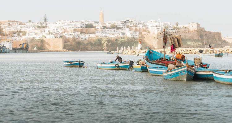 Petites barques de pêche bleues sur une rivière calme avec la kasbah historique de Rabat en arrière-plan.