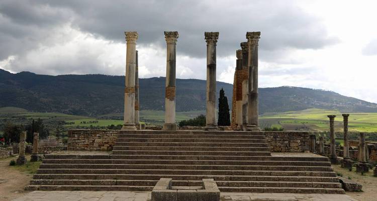 Colonnes romaines isolées sur plateforme à gradins à Volubilis avec ciel dramatique.