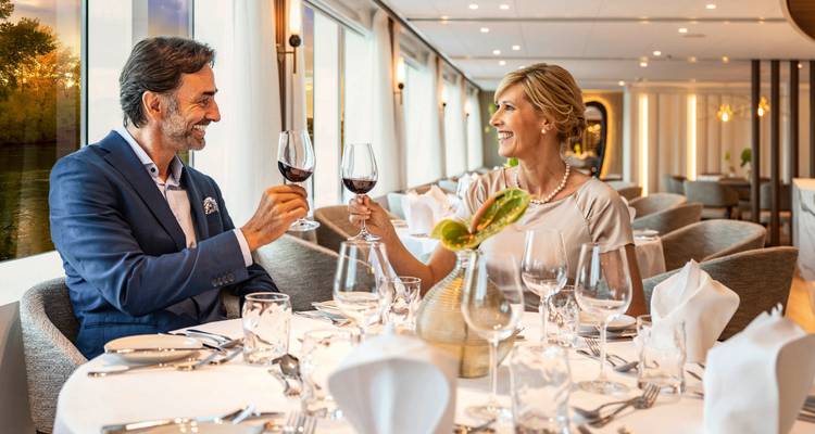 Elegantes Paar, das Rotweingläser in einem hellen Speisesaal eines Flusskreuzfahrtschiffs anstößt