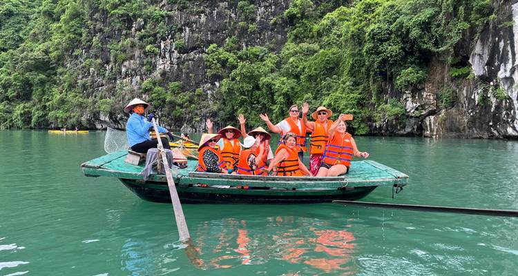 Gruppe von Reisenden in Schwimmwesten lächelt von einem grünen Holzboot auf türkisfarbenem Wasser der Halong-Bucht.